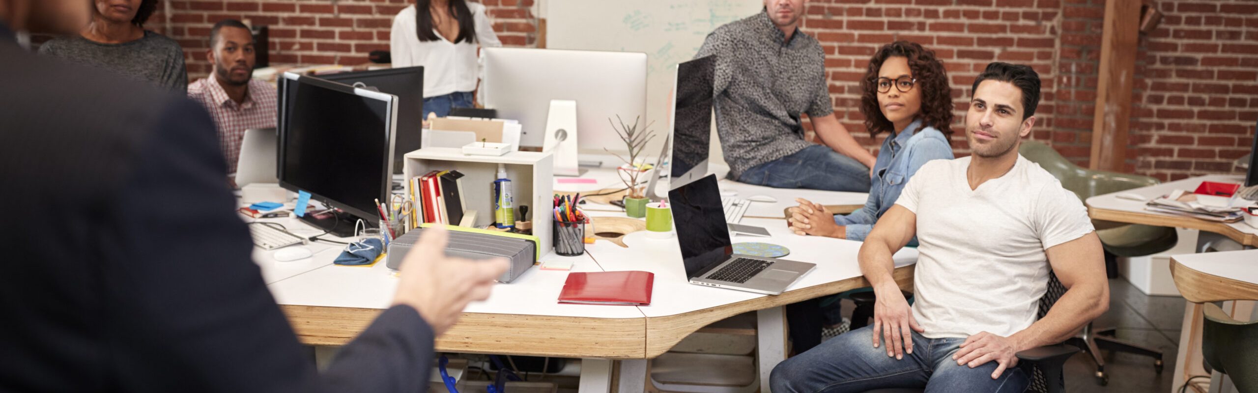 Senior Businessman Talking At Meeting Of Casually Dressed Business Team In Open Plan Office